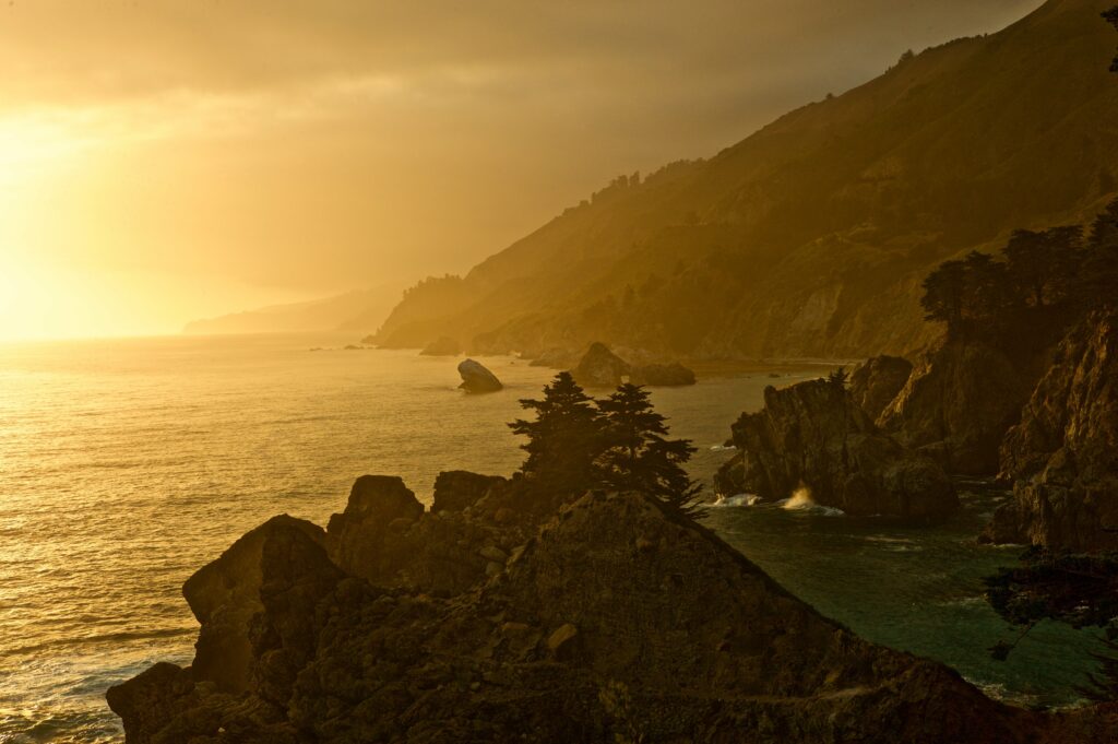 Tranquil coastal sunset with golden light on rugged sea rocks and steep cliffs at dusk Wallpaper