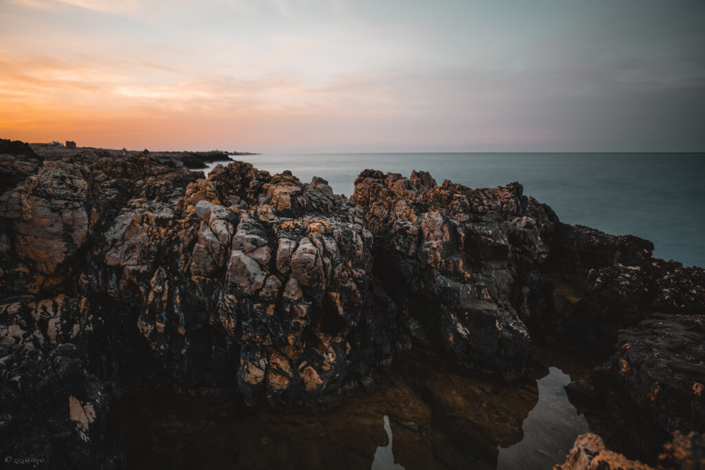 Sunset coastline with rugged rocks calm sea and glowing sky in warm earthy tones wallpaper
