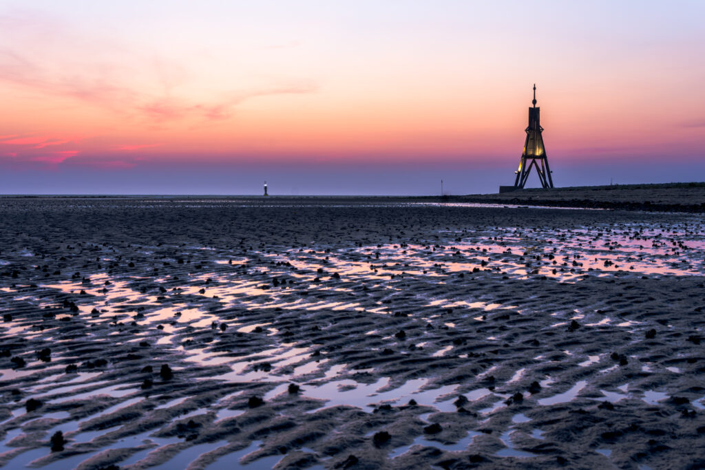 Coastal tower at twilight on serene beach with textured sand ripples and colorful sky reflection Wallpaper
