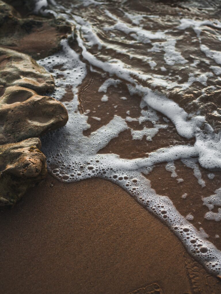 Tranquil coastal wallpaper with rugged rocks gentle sea foam on smooth brown sand in soft light