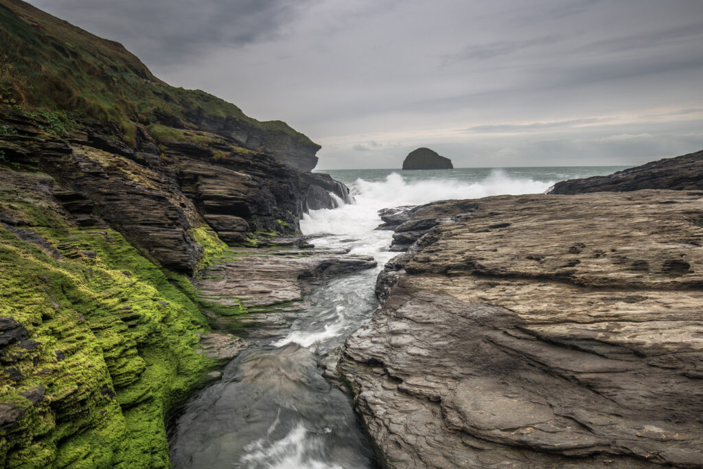 Rugged coastal rocks with green moss and restless waves under overcast sky wallpaper background