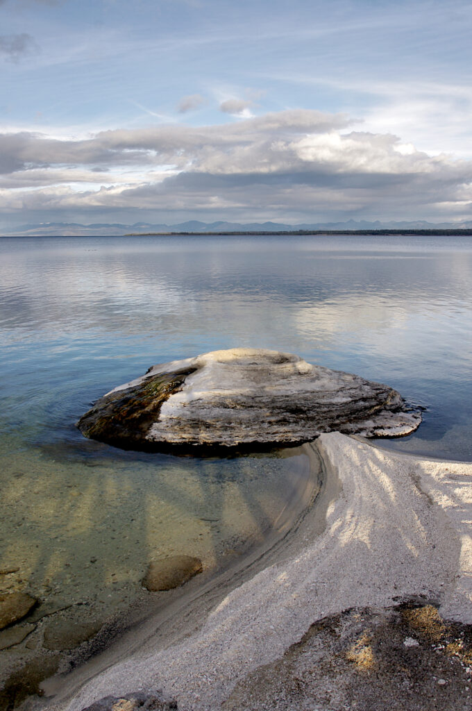 Tranquil coastal wallpaper with smooth stone on sandy shore gentle sea ripples and cloudy sky