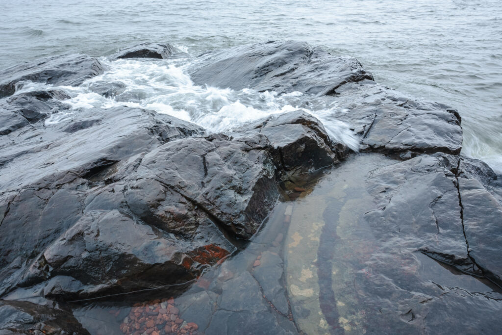 Smooth dark coastal rocks washed by gentle sea waves with glistening textures under soft light Wallpaper