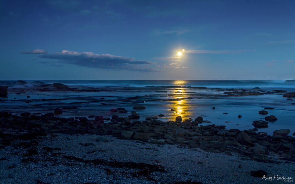 Tranquil coastal wallpaper with smooth stones golden sunset and partial eclipse over calm sea