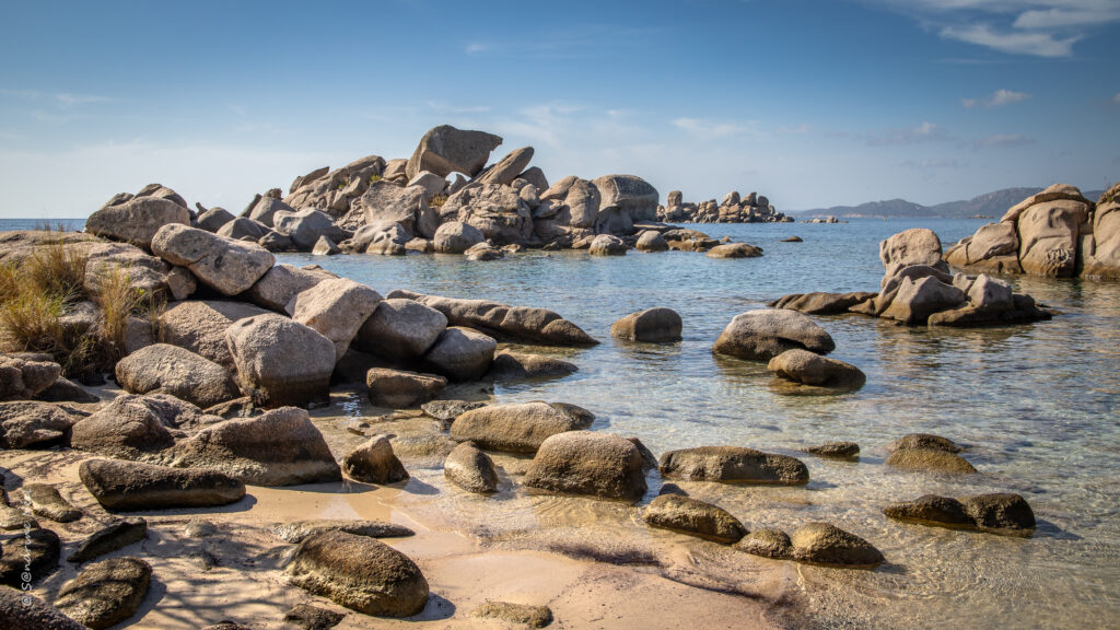 Tranquil coastal wallpaper with smooth stones on sandy shore and clear blue sea under bright sky