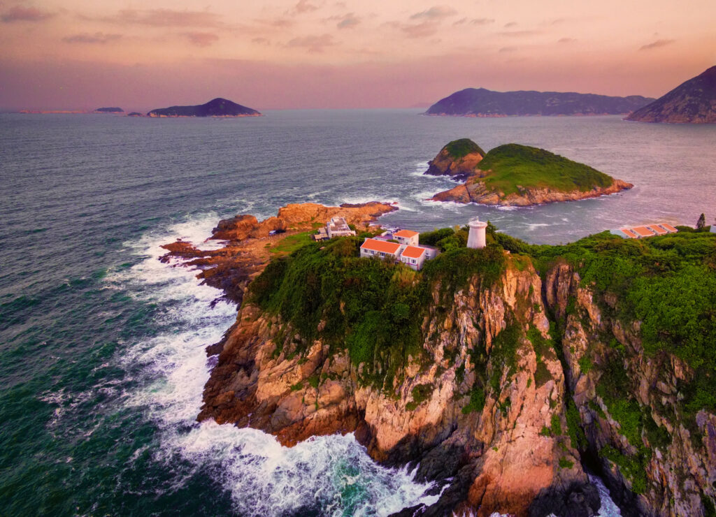 Coastal wallpaper with rugged cliffs white lighthouse green islands crashing waves colorful dusk sky