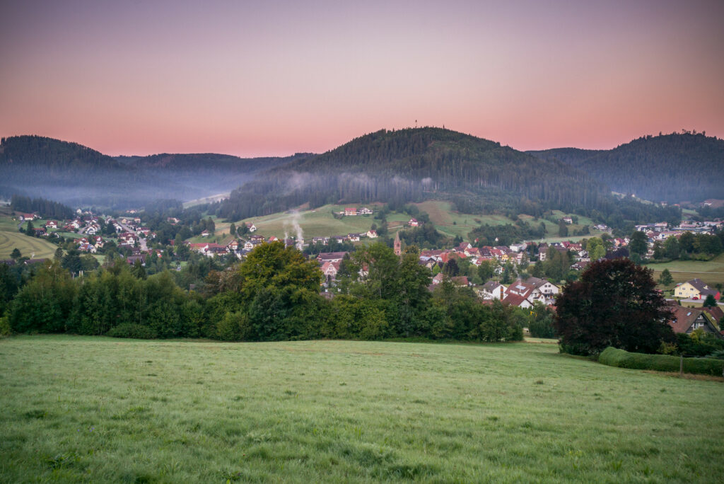 Tranquil countryside village between green hills with pink purple morning light wallpaper background