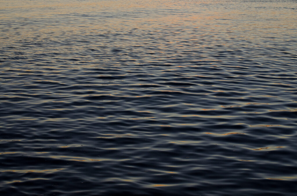 Tranquil dark sea water wallpaper with gentle ripples and soft evening light reflections