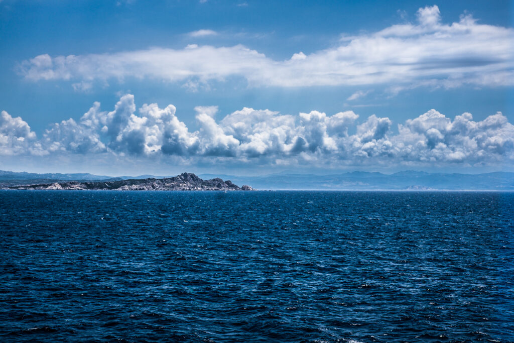 Vivid seascape with deep blue water rocky mountains and dramatic clouds under bright sky wallpaper