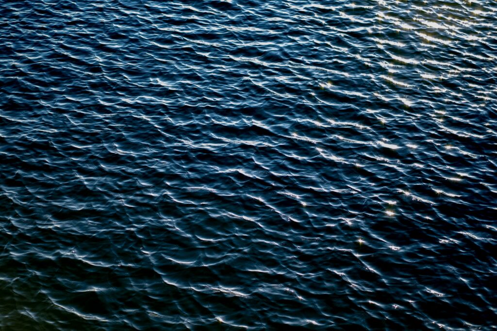 Tranquil deep blue water surface with gentle ripples and light reflections wallpaper background