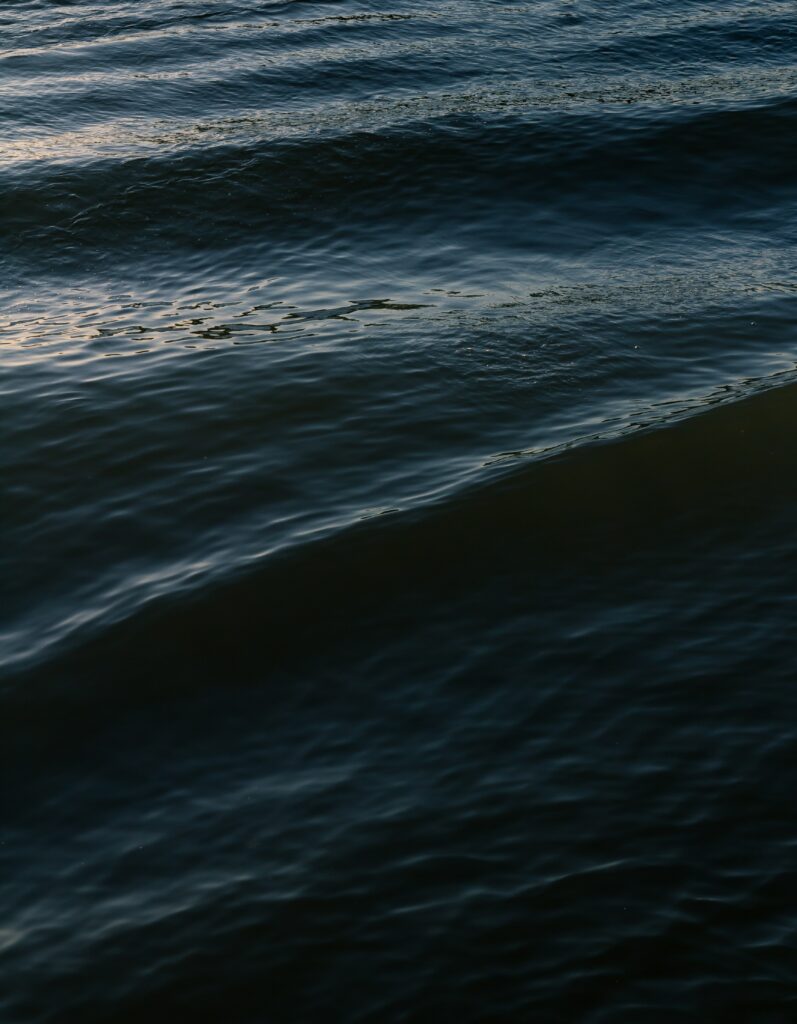 Dark tranquil water surface with gentle waves and deep blue ripples serene wallpaper background