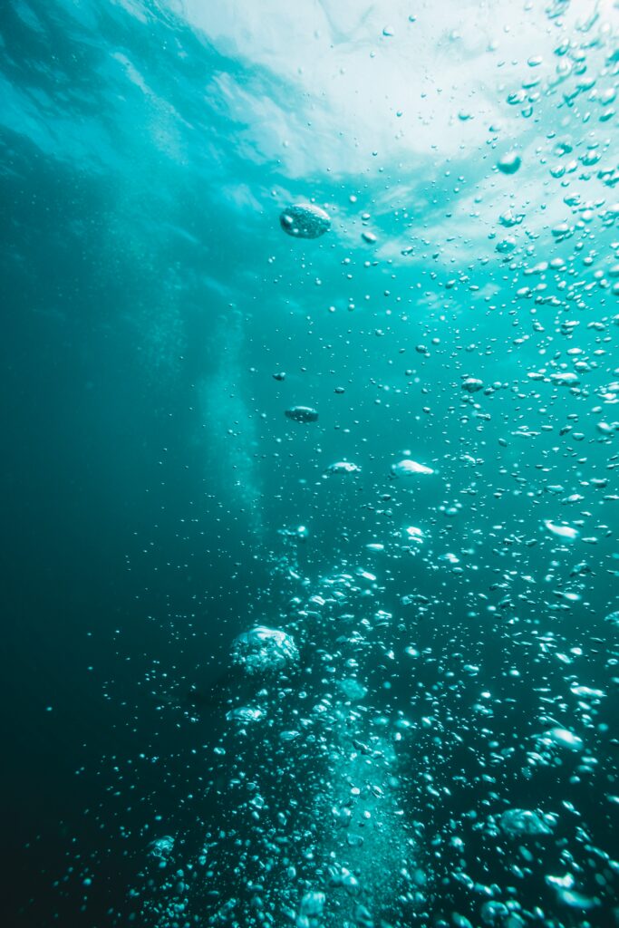 Tranquil deep water wallpaper with teal blue shades light rays and rising bubbles background