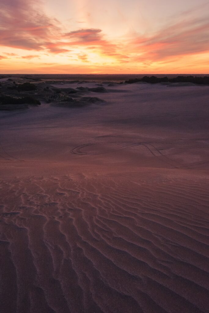 Tranquil desert landscape at twilight with sand ripples bushes and vibrant orange pink purple sunset Wallpaper