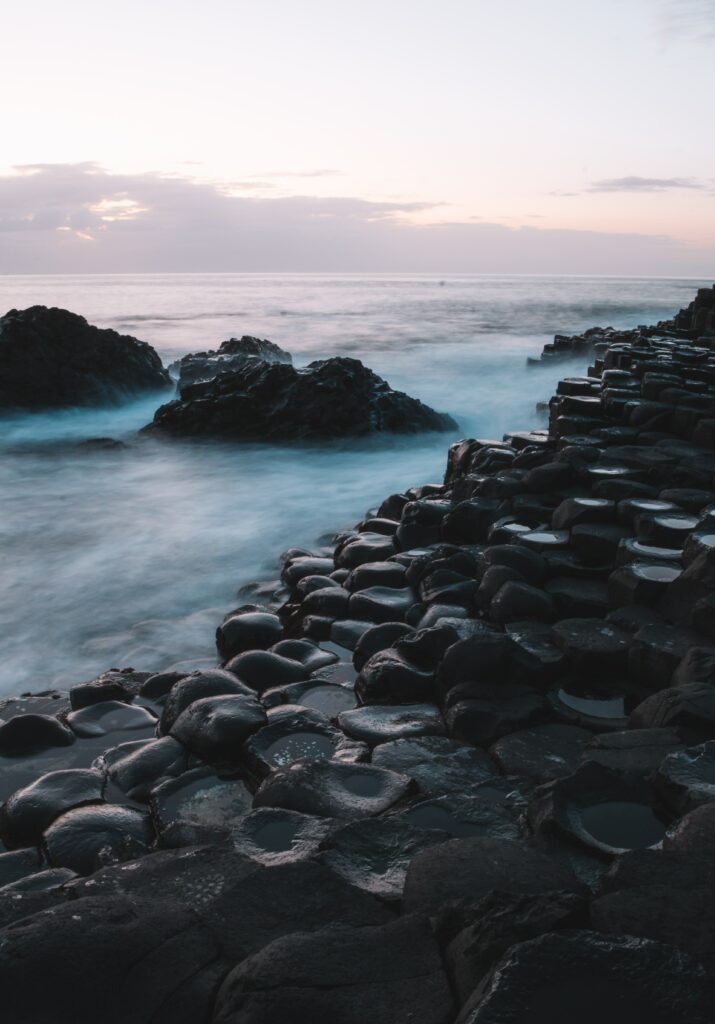 Tranquil dusk coastline with hexagonal basalt rocks and misty sea water in soft pastel hues Wallpaper