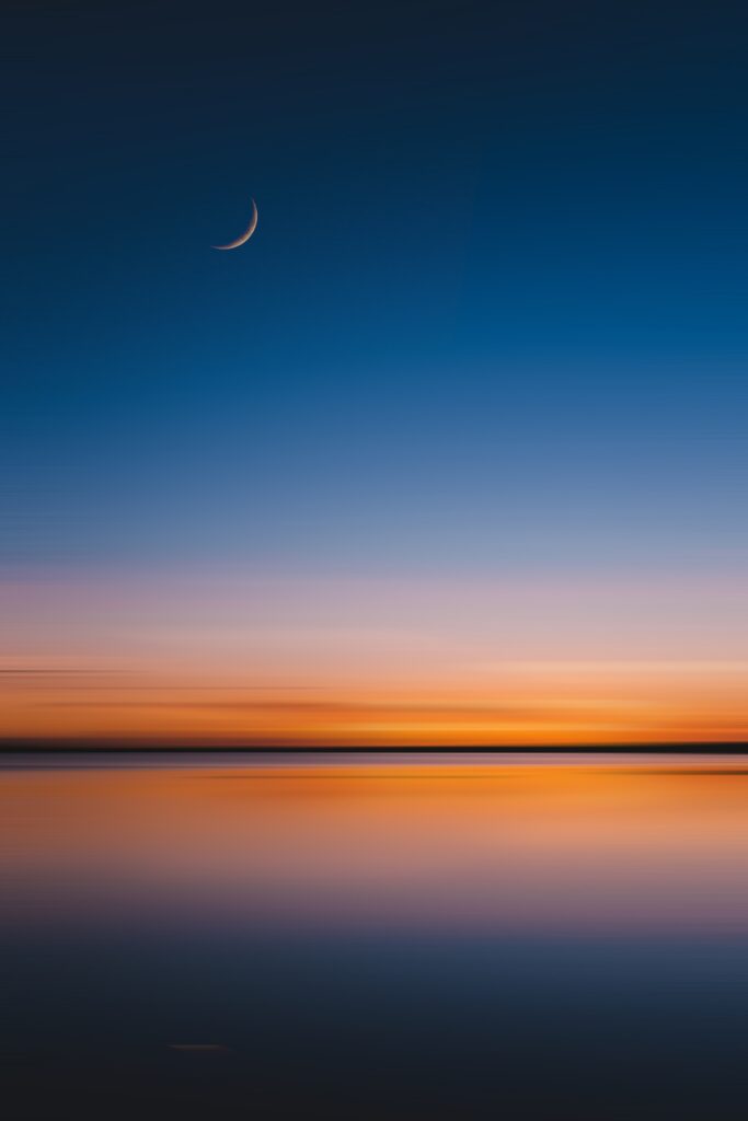 Serene dusk wallpaper with crescent moon over calm water and soft orange purple horizon hues