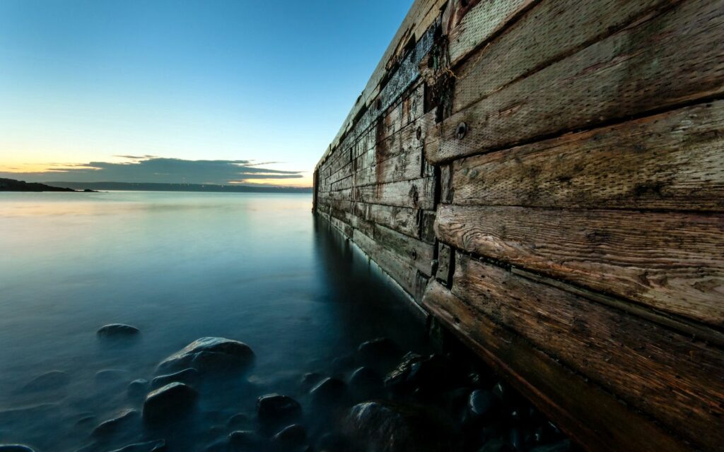 Tranquil lake at dusk with old wooden bridge reflecting soft blue and golden tones wallpaper