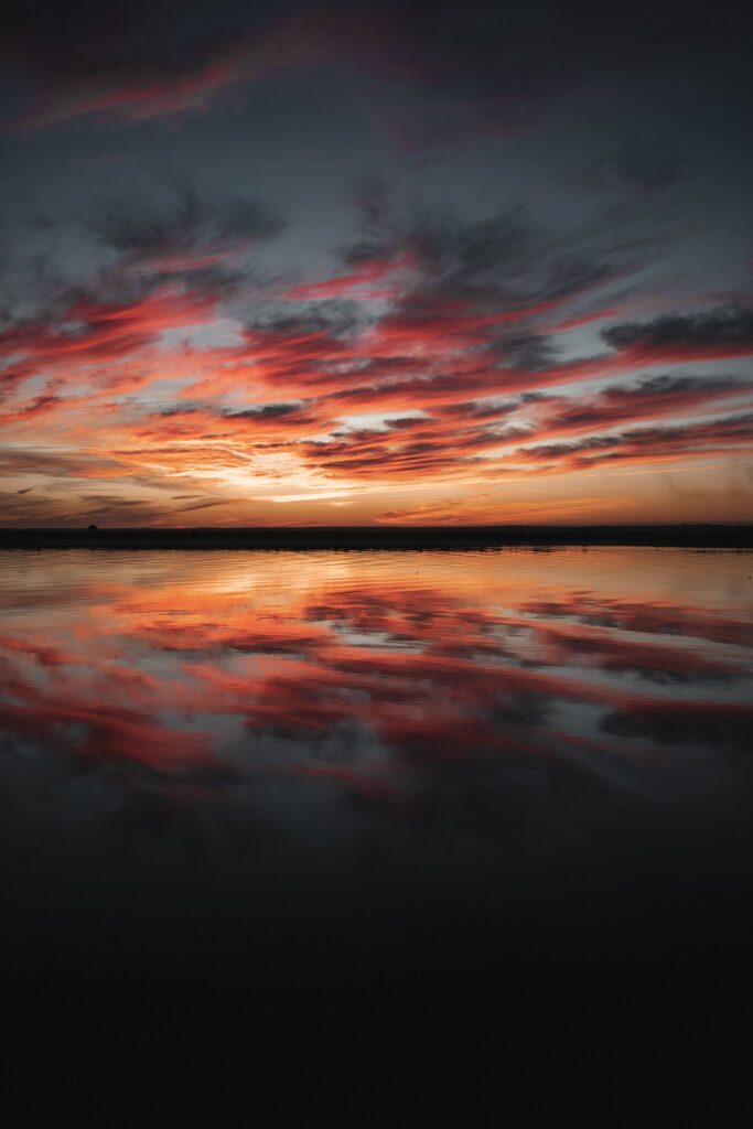 Dusk wallpaper with vibrant red and orange clouds reflected on calm water in serene nature