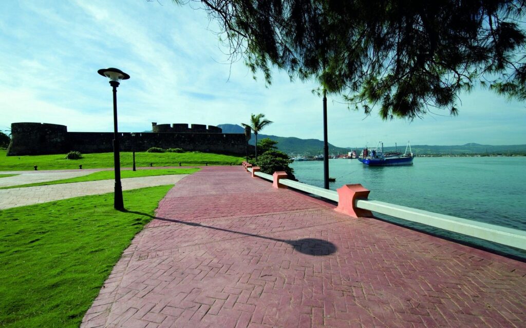 Tranquil embankment with brick pavement solar lamps lush grass moored ship distant mountains wallpaper