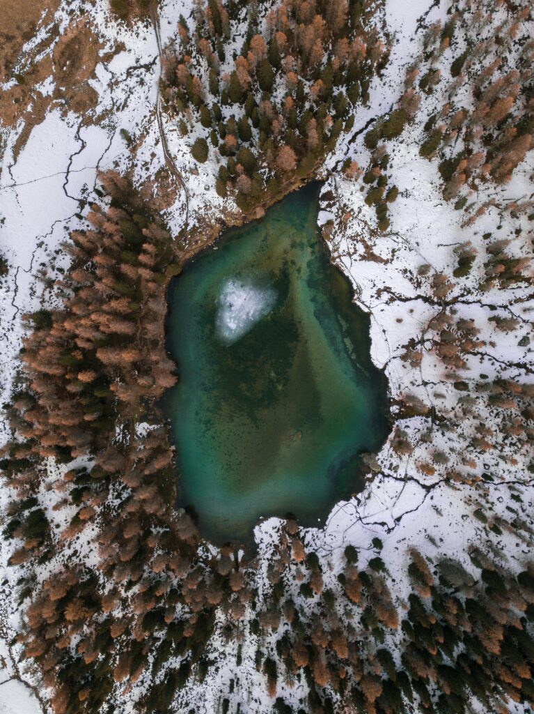 Aerial view of emerald green lake surrounded by snow-dusted trees winter landscape wallpaper background