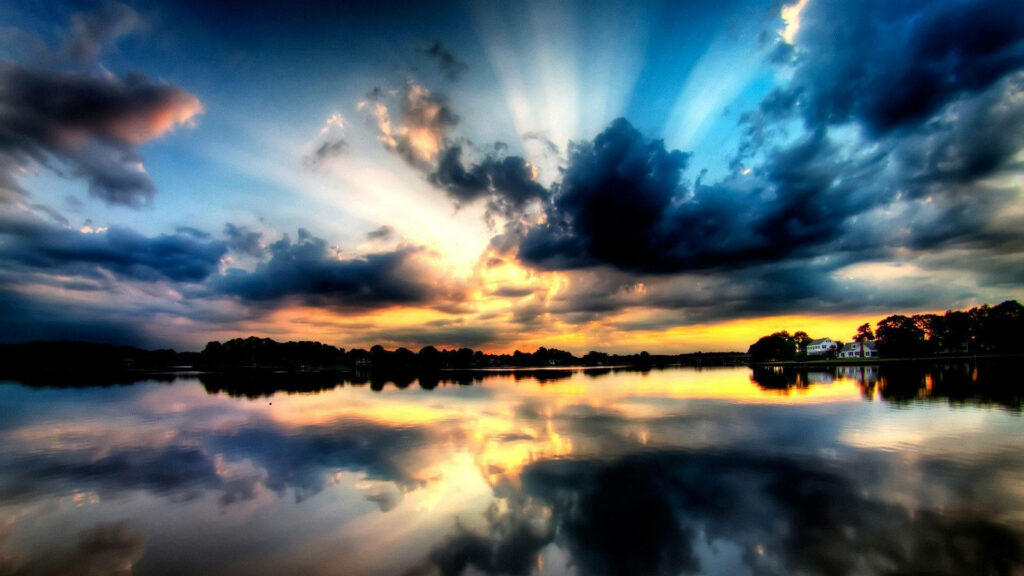 Dramatic sunset over calm lake with golden reflections silhouetted trees and cottages horizon Wallpaper