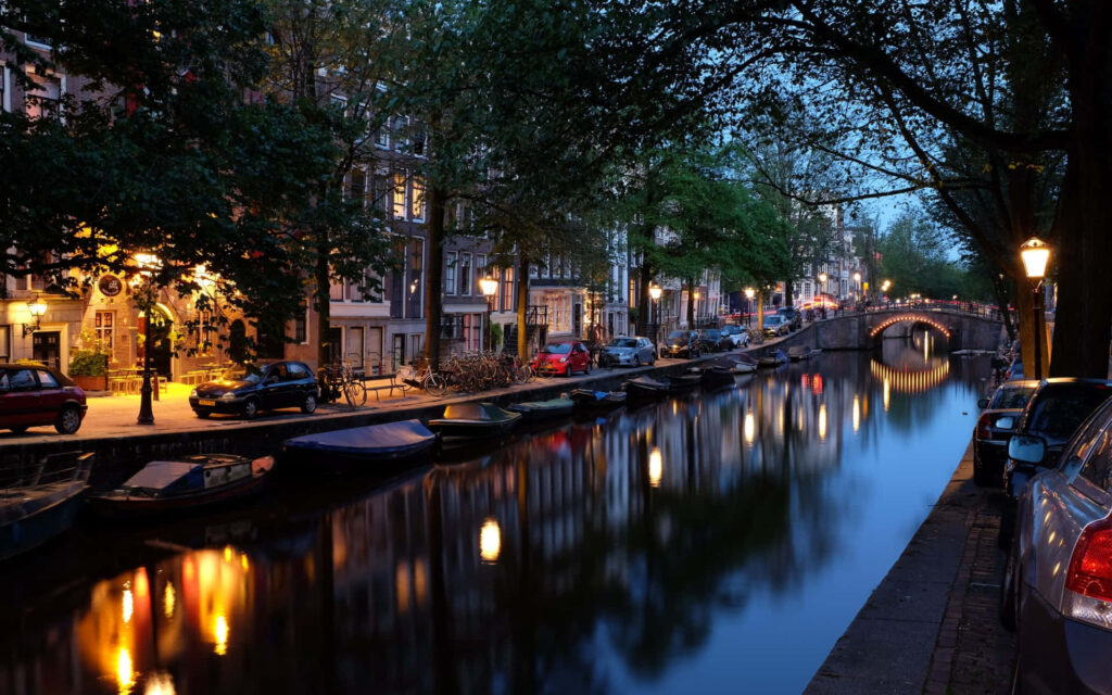 Tranquil evening canal in Alkmaar with warm streetlights reflecting and charming houses lining street Wallpaper