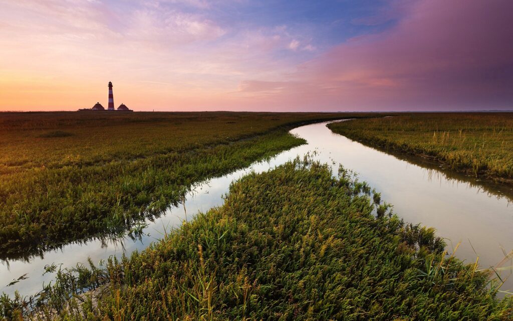 Tranquil sunset over winding irrigation channel through green field with distant beacon landmark Wallpaper