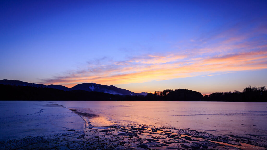 Serene evening lake wallpaper with calm waves rolling hills and vibrant blue orange sky reflection