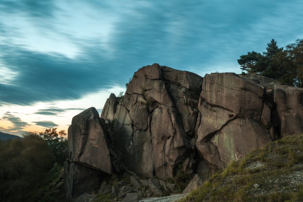 Towering rocks in evening light with dramatic clouds and trees serene natural landscape wallpaper