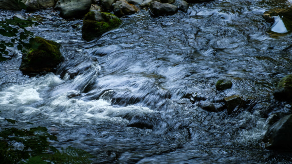Tranquil flowing stream over smooth stones with blue and green hues nature wallpaper background