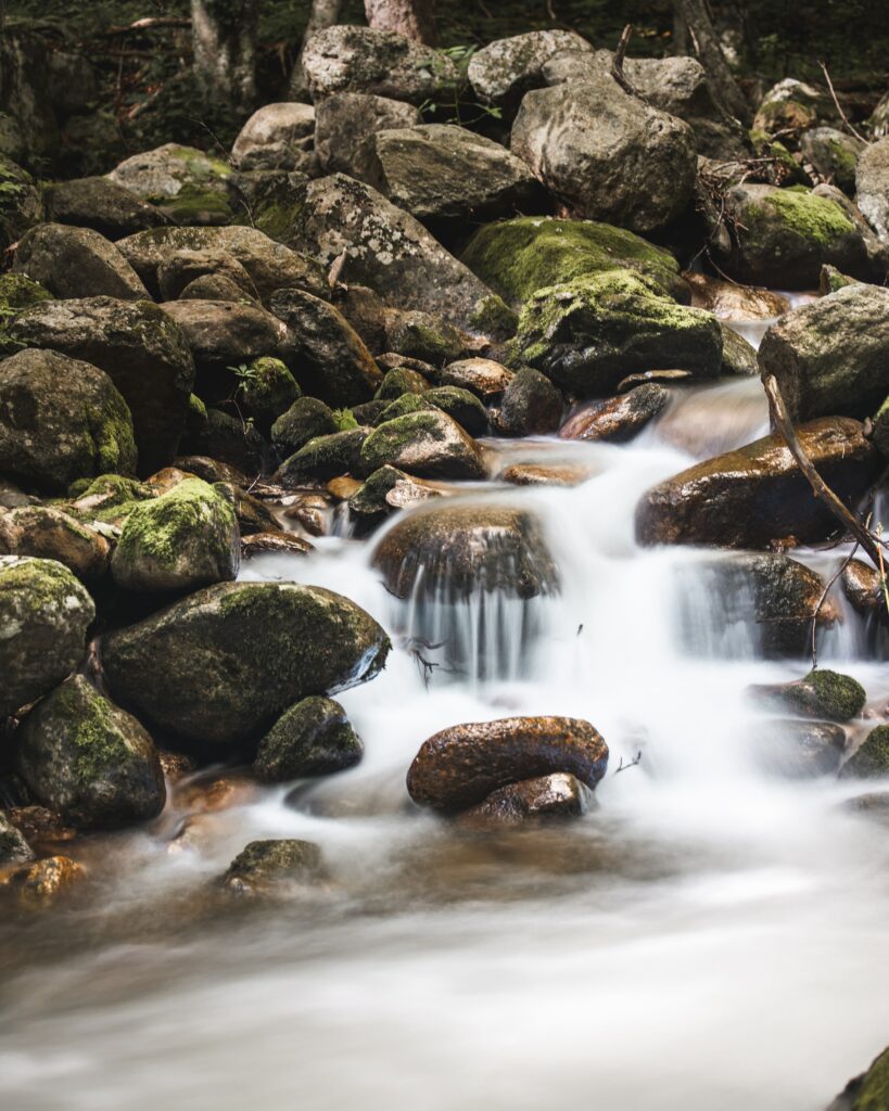 Serene river with smooth flowing water mossy stones lush green forest long exposure wallpaper background