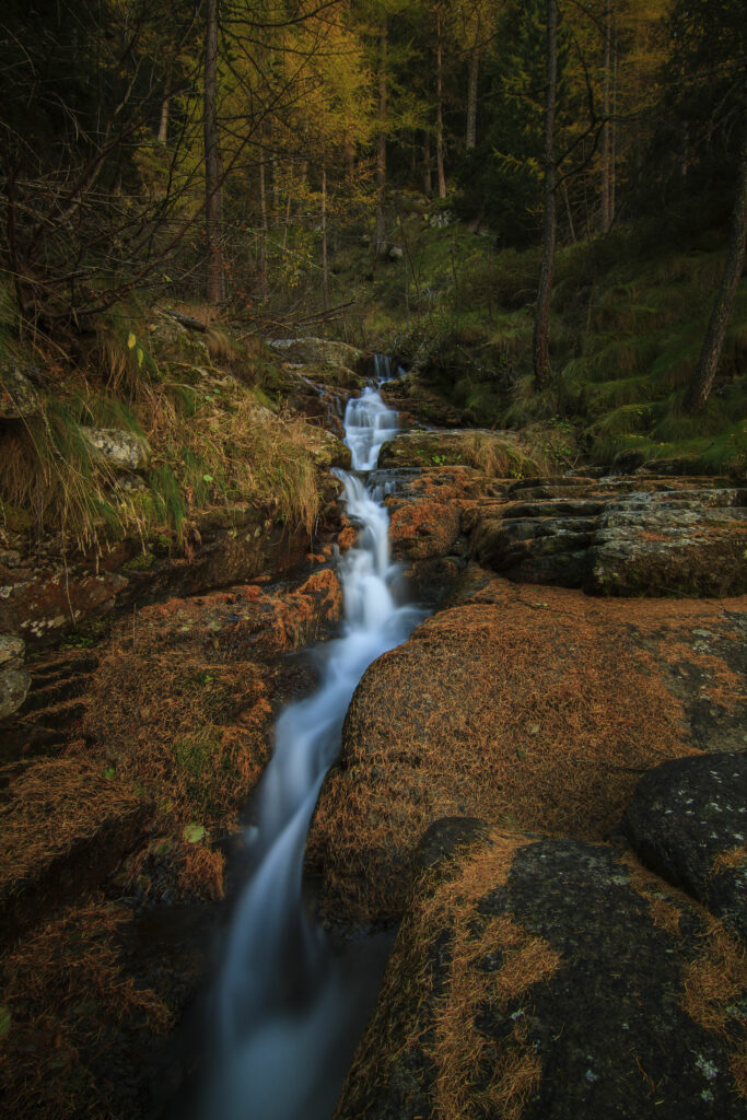 Tranquil forest waterfall with gentle stream over stones surrounded by autumn foliage wallpaper