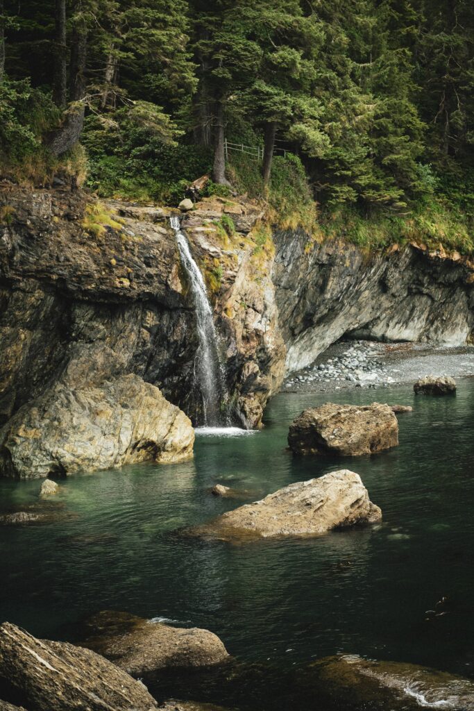 Serene waterfall cascading over rocks into clear pool surrounded by lush green forest trees wallpaper