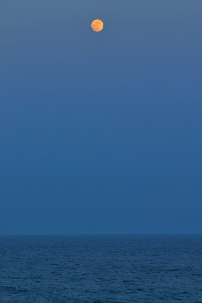 Glowing full moon over calm sea under clear blue night sky minimalist peaceful wallpaper background