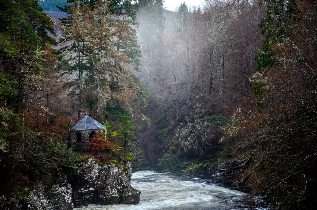 Charming gazebo on rocky cliff overlooking rushing river surrounded by dense forest and mist Wallpaper