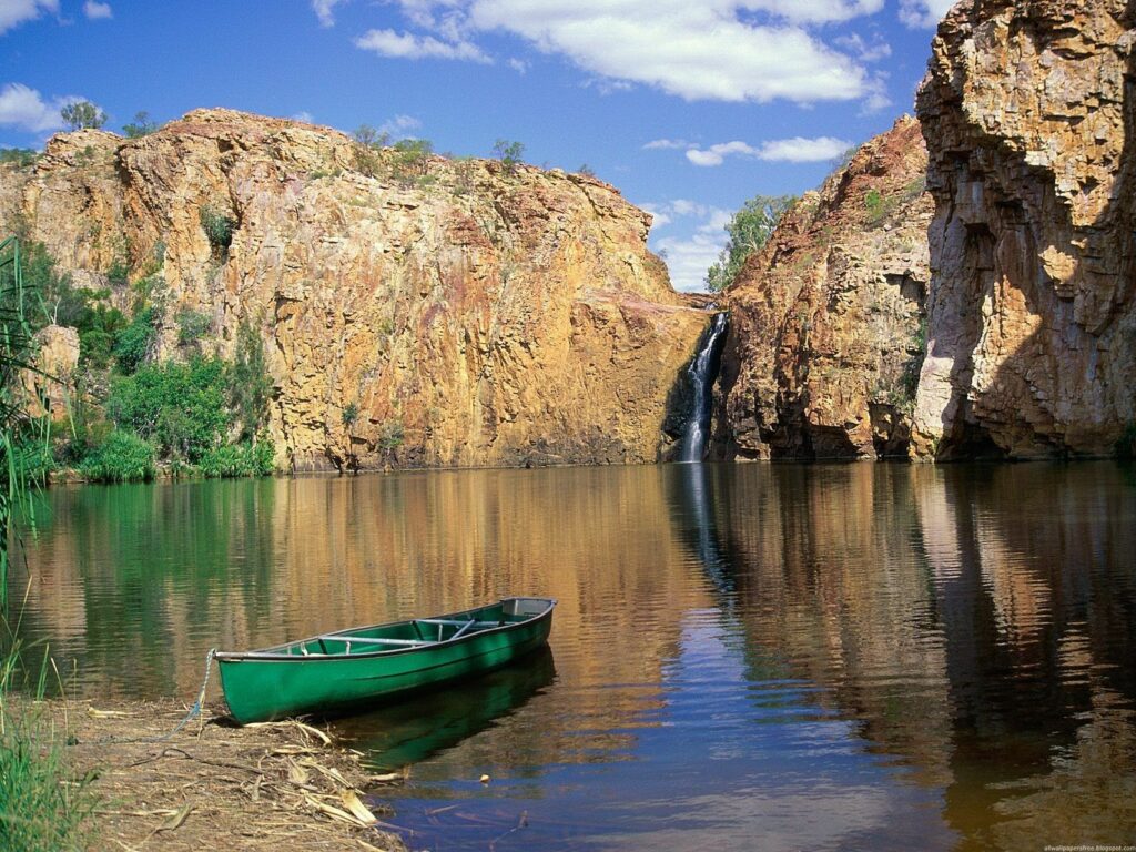 Tranquil green boat on calm lake waters with Australian cliffs and waterfall under blue sky wallpaper