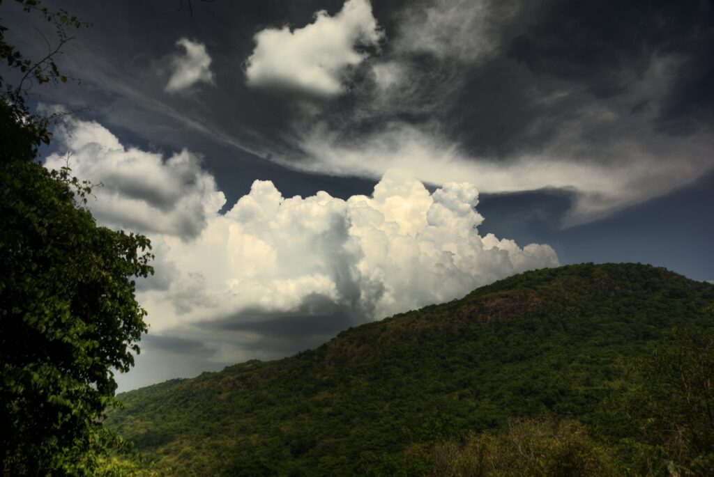Lush green hill landscape with dramatic white clouds and vibrant greenery under soft light Wallpaper