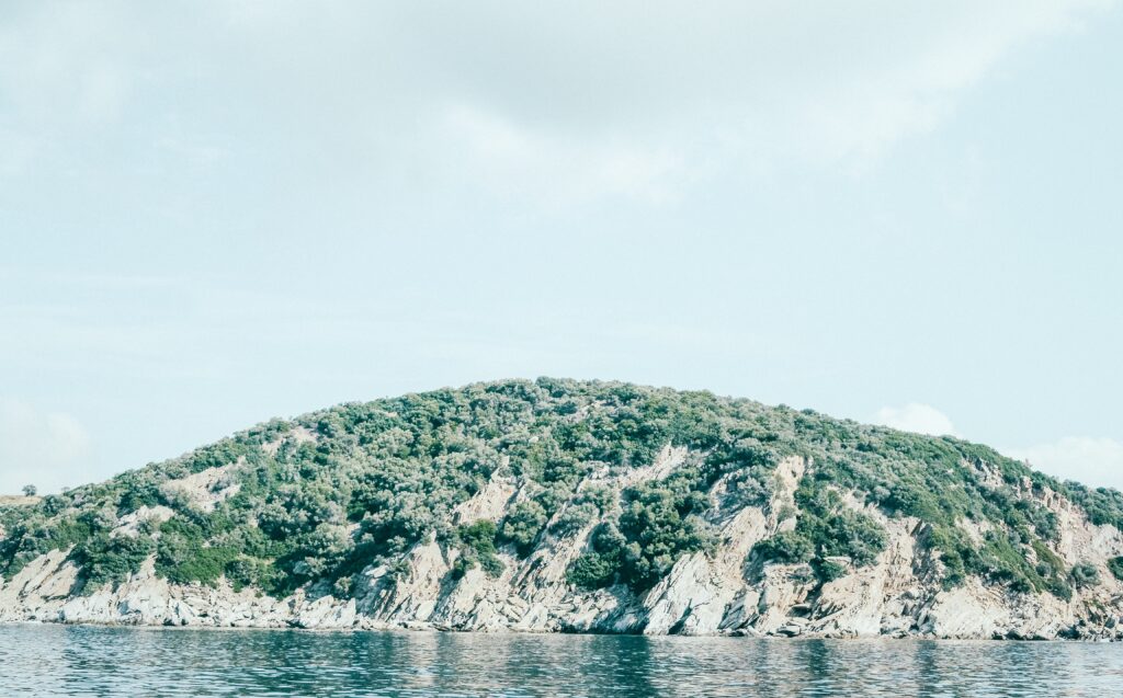 Tranquil island with lush greenery and calm reflective sea under soft cloudy sky wallpaper
