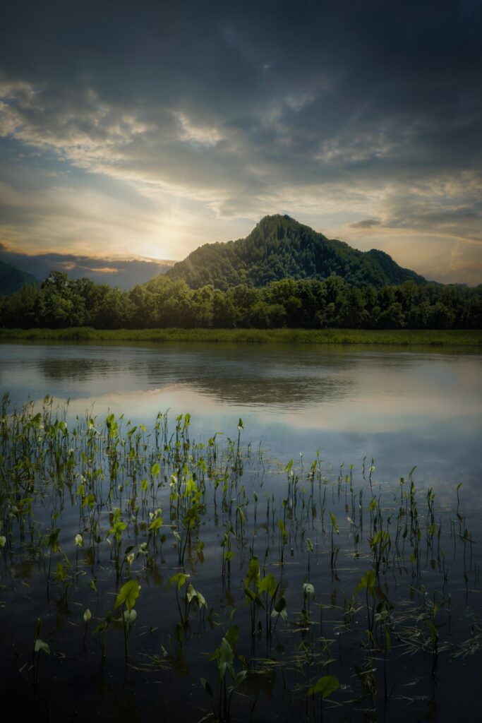 Serene mountain landscape with lush trees and calm lake reflecting sunset and cloudy sky wallpaper