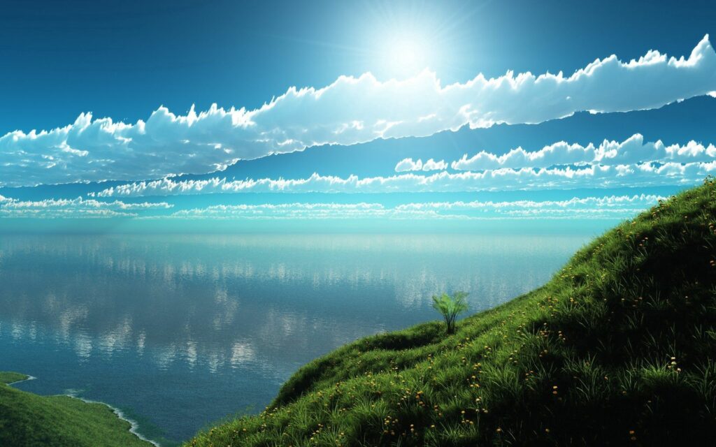 Lush green slope with wildflowers by calm reflective water under bright blue sky and clouds wallpaper