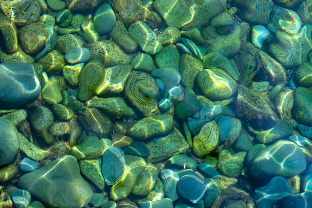 Smooth green stones submerged in clear water with sunlight reflections creating a calming scene Wallpaper