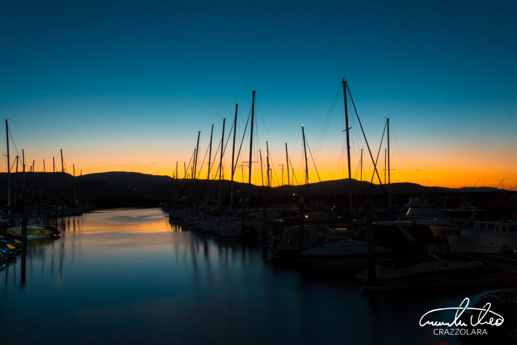 Tranquil sunset harbor scene with docked boats yachts calm water and vivid colorful sky background Wallpaper