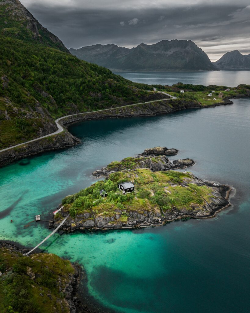 Aerial view of tranquil island in turquoise lake surrounded by green mountains under cloudy sky Wallpaper