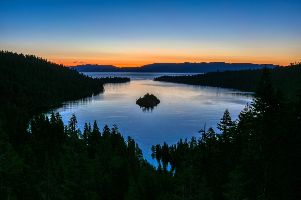 Tranquil island on serene lake with dense forest and mountains at vibrant sunset wallpaper background