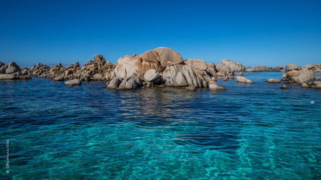Tranquil lagoon with clear blue water and rugged coastal rocks under a clear sky wallpaper