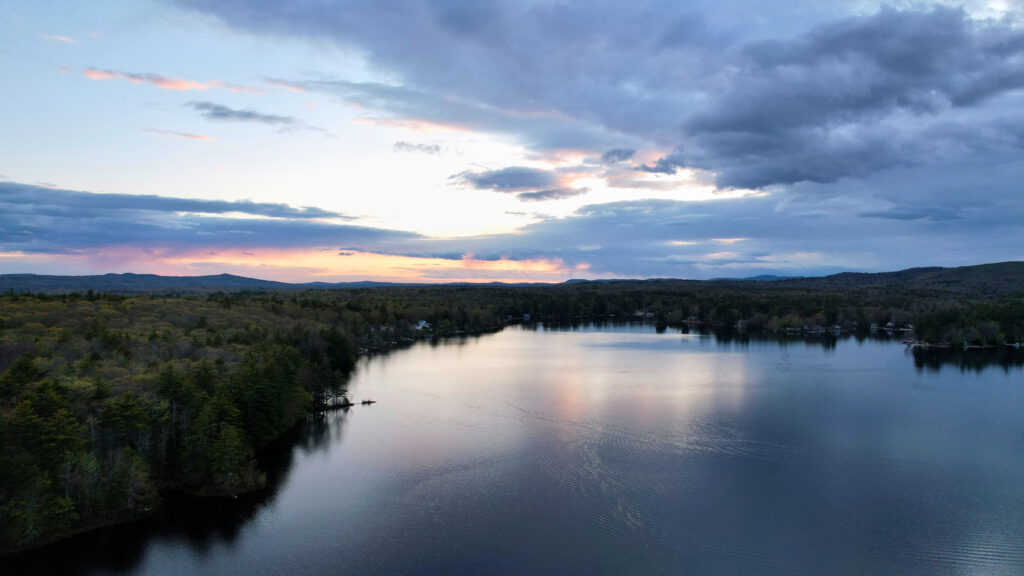 Aerial view of tranquil lake surrounded by green trees reflecting colorful dawn sky wallpaper background
