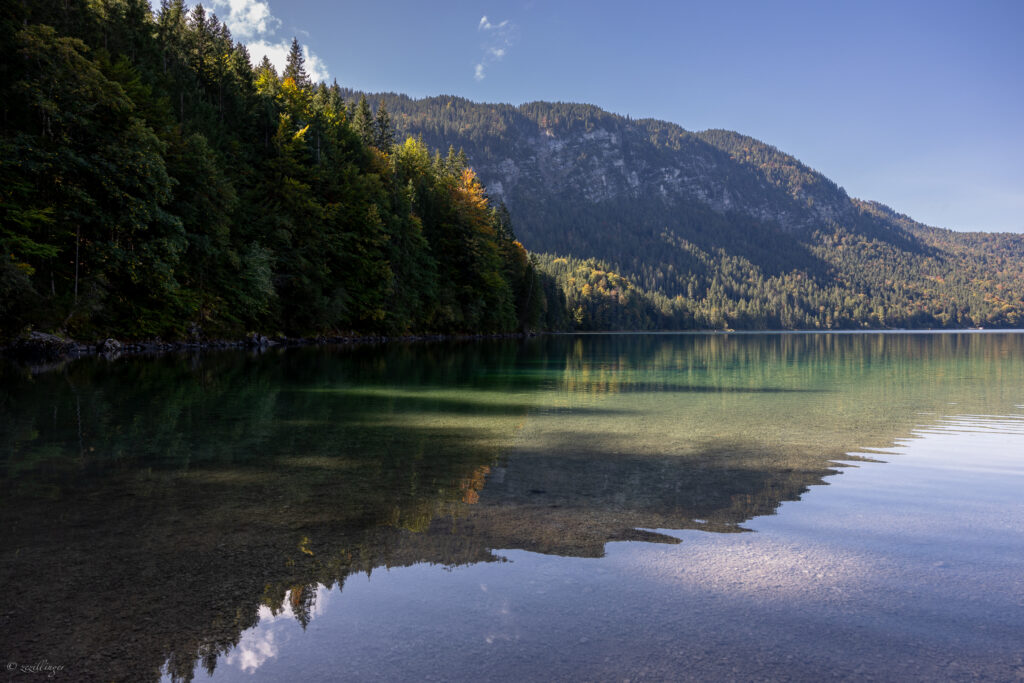 Tranquil lake reflecting lush green trees and towering mountains under a clear blue sky wallpaper