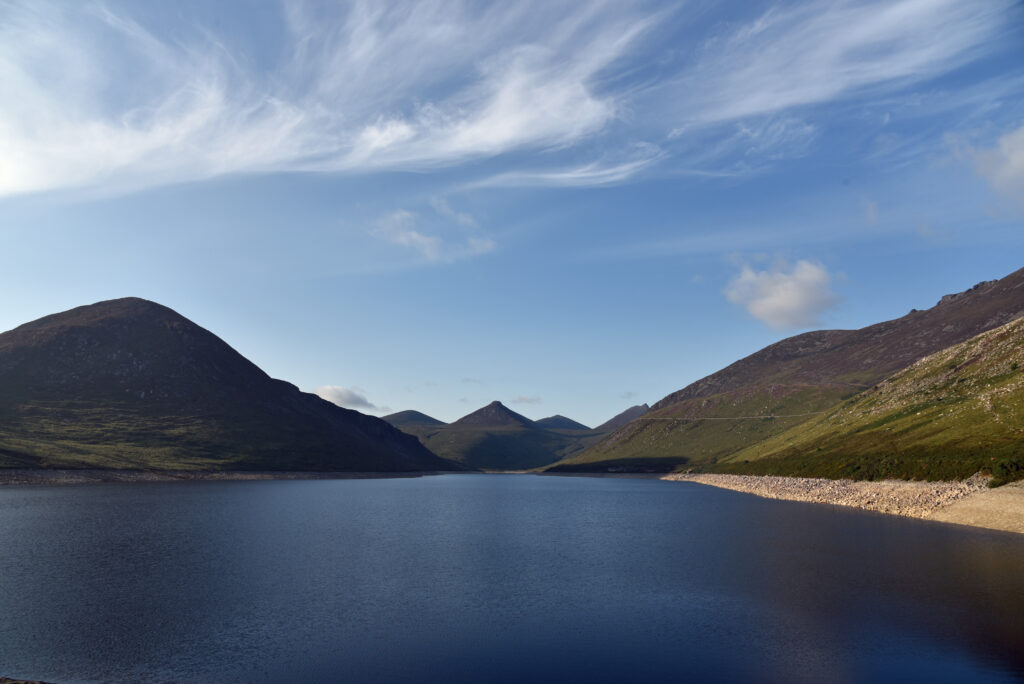 Tranquil lake reflecting hills and mountains under a vast blue sky serene nature wallpaper background