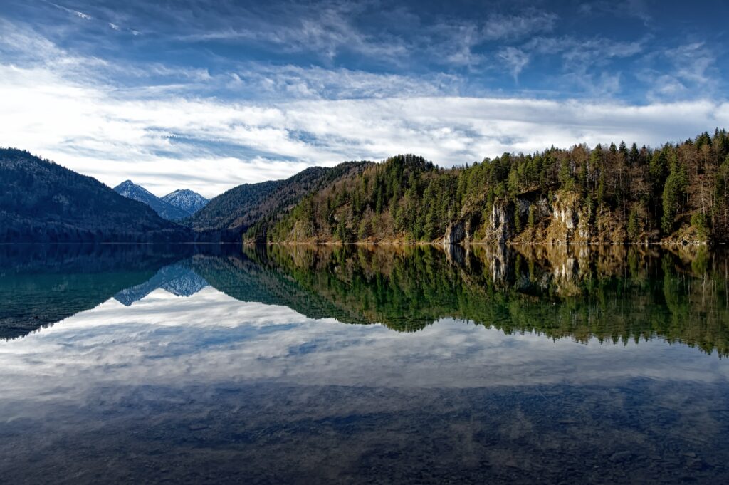 Tranquil lake reflecting mountains dense forests and blue sky serene nature landscape wallpaper