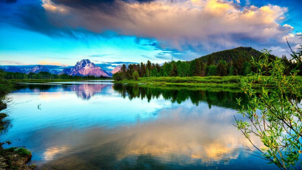 Tranquil lake reflecting vibrant sky mountains clouds lush green trees bright sunlight wallpaper
