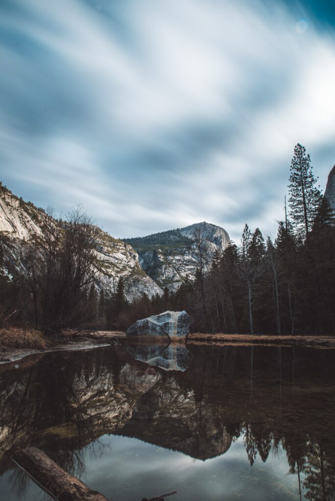 Tranquil lake reflecting rocky cliffs and evergreen trees under soft cloudy sky wallpaper background